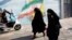 Iranian women walk next to a wall painting of Iran’s national flag in a street in the capital, Tehran. (file photo)