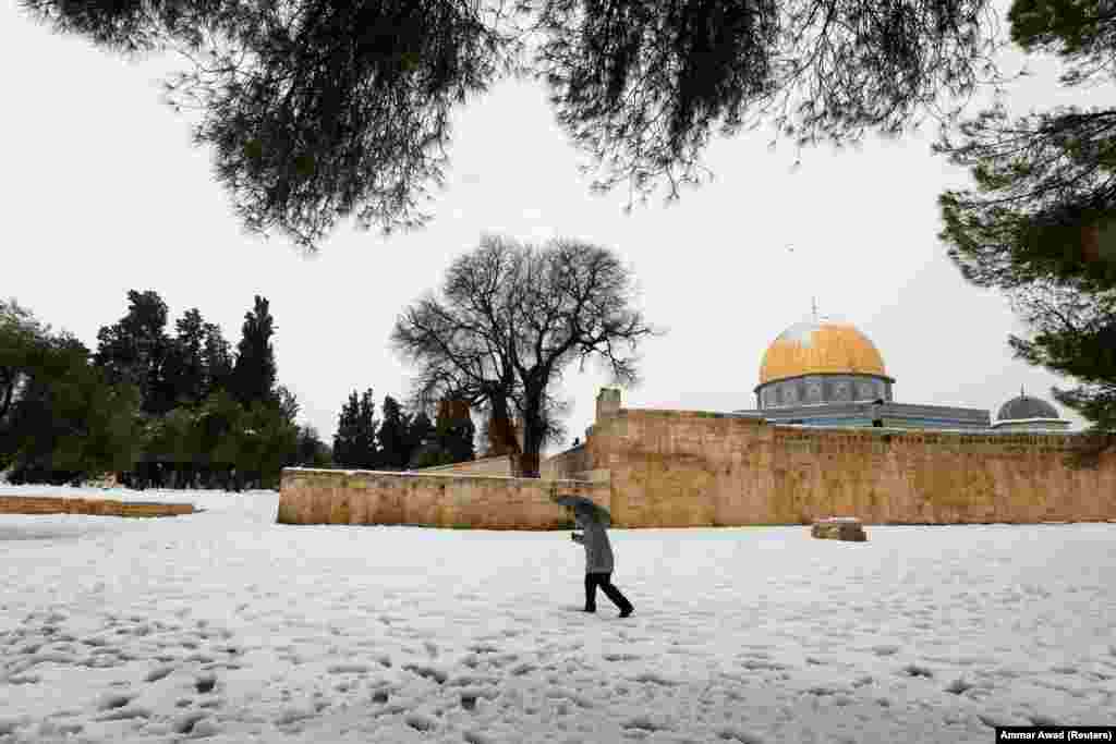 Një burrë duke ecur pranë Kupolës së Shkëmbit, që ndodhet në qytetin e vjetër të Jerusalemit gjatë një mëngjesi me borë.