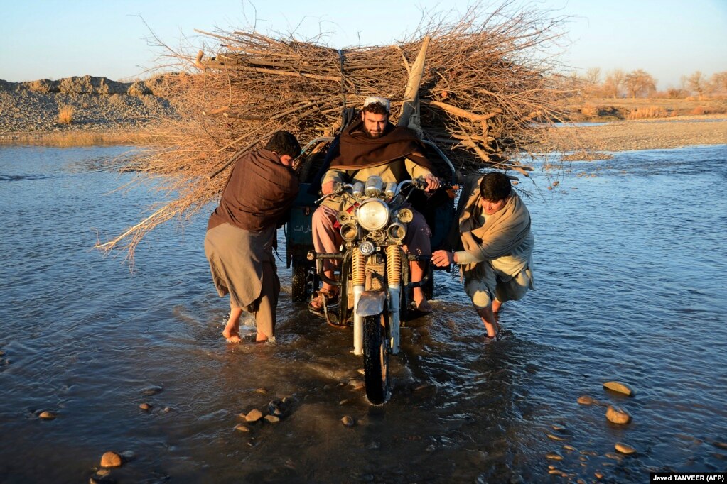 Disa burra duke kaluar lumin Arghandab, me një motoçikletë me tri rrota, të ngakuar me një grumbull degësh, në periferi të Kandaharit, në Afganistan, më 24 janar.