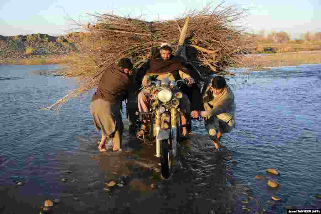 Un grup de bărbați traversează râul Arghandab pe o bicicletă cu trei roți încărcată cu crengi, la periferia orașului Kandahar, Afganistan, 24 ianuarie 2022. &nbsp;