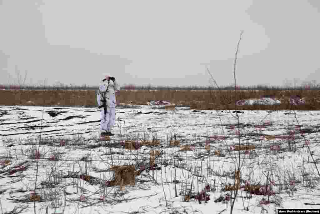 Боєць Збройних сил України у зимовому камуфляжі оглядає позиції підтримуваних Росією бойовиків. Донецька область, Україна. 21 січня 2022 року