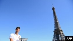 Novak Đoković a Roland Garroson elnyert trófeával pózol a párizsi Eiffel-torony előtt 2021. június 14-én