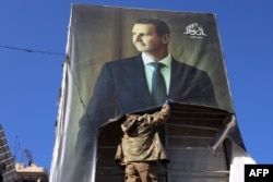 Një luftëtar antiqeveritar duke larguar një poster të presidentit sirian, Bashar al-Assad. Alepo, 30 nëntor 2024.