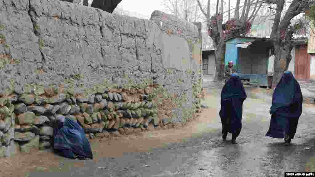 Femei îmbrăcate în burqa trec pe lângă o femeie bolnavă în localitatea Fayzabad, provincia Badahșan, Afganistan.
