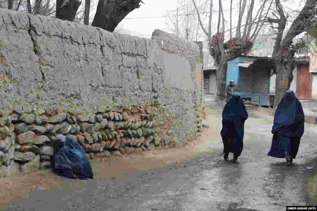 Burqa-clad women walk past a sick woman along a road in the Fayzabad district of Badakhshan Province.