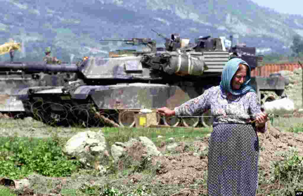 An Albanian woman spins wool in front of a U.S. M1 Abrams tank that was part of NATO&#39;s operation during the Kosovo conflict, outside the Rinas airbase on May 12, 1999. With a crew of four (commander, gunner, loader, and driver), the Abrams is one of the heaviest tanks in service at nearly 62 metric tons. &nbsp;