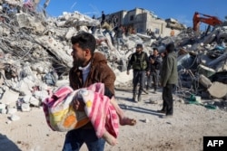 Мъж носи тялото на дете, извадено от развалините в град Харим в провинция Идлиб, контролирана от бунтовниците в Сирия, 8 февруари 2023 г.