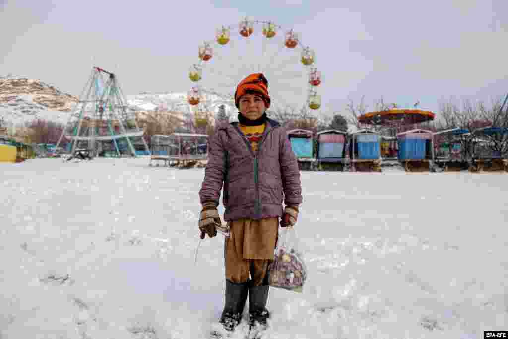 An Afghan boy poses for a photograph outside a snow-covered amusement park in Kabul.
