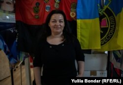 Леся Копчук на тлі прапорів та шевронів, які їй подарували українські військові