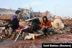 Люди сидят среди развалин своих домов после землетрясения в турецкой провинции Хатай. 7 февраля 2023 года