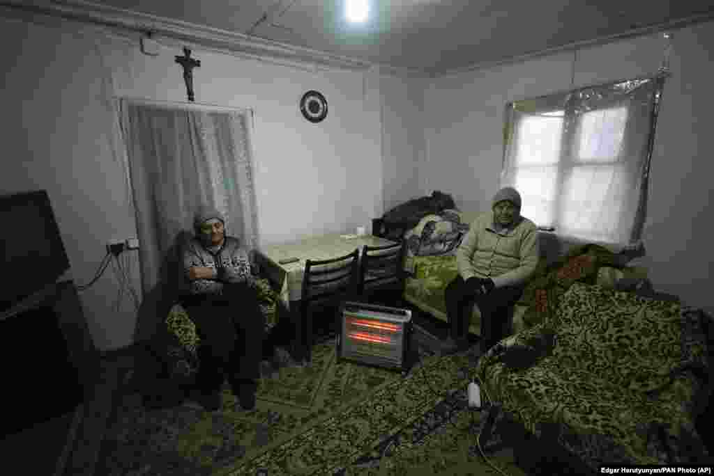 Two elderly women warm themselves near a heater in Stepanakert. &nbsp;