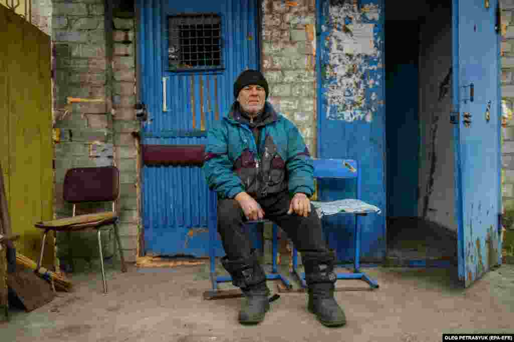 Volodymyr sits next to the entrance to his apartment building, where he and three neighbors live in the basement. He spends his time chopping the wood that the residents need to stay warm.