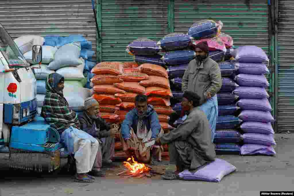 Laborers keep themselves warm near a fire as they wait for work on a cold morning at the wholesale grain market in Karachi, Pakistan.&nbsp;