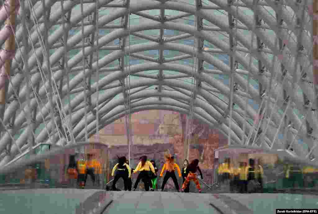 Дзяўчыны танчаць на пешаходным мосьце ў дажджлівы дзень у Тбілісі. (epa-EFE/Zurab Kurtsikidze)