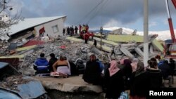  Люди сидят перед разрушенным зданием после землетрясения в Газиантепе, Турция, 7 февраля 2023 года.