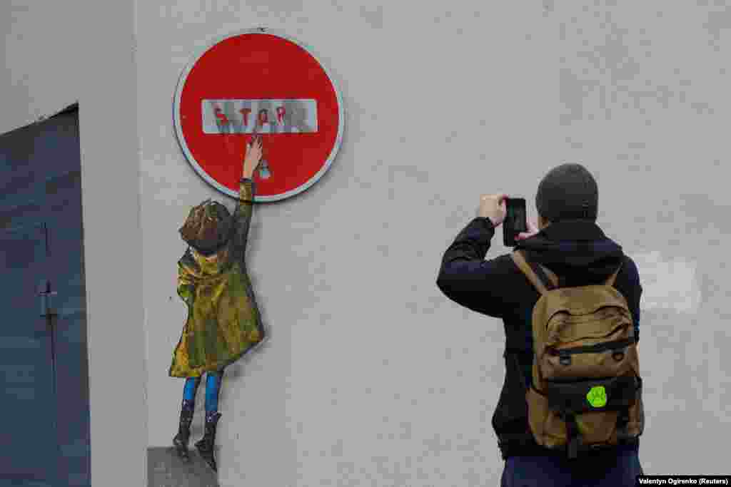 Чоловік фотографує малюнок відомого вуличного художника Tvboy на стіні будівлі в центрі Бучі, 29 січня 2023 року