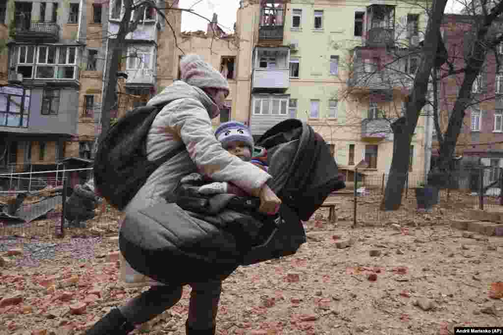 A woman carries her child as they evacuate from a residential building that was hit by a Russian rocket in the center of the Ukrainian city of Kharkiv.