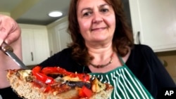 Тицијана ди Костанцо, ко-основачка на Хоризон инсектс, во нејзината кујна во Лондон, покажува парче пица чие тесто е направено од прав од мелени штурци