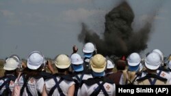 Ukrán tűzszerészek egy robbanást néznek egy aknamezőn Kambodzsában 2023. január 19-én. Tizenöt ukrán tűzszerészt képeznek ki Kambodzsában szakértők, akik a világ legjobbjai között vannak a közel három évtizedes háború nyomainak felszámolásában szerzett tapasztalataik miatt