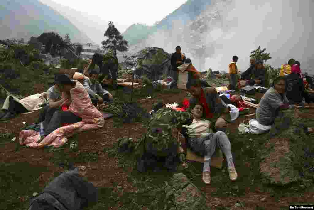 Раненые жертвы смертоносного землетрясения в провинции Сычуань днем ранее сидят на развалинах в ожидании помощи в Бэйчуане, Китай, 13 мая 2008 года. В результате землетрясения магнитудой 7,9 погибло более 87 500 человек.