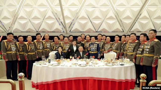 Kim Jong Un, gruaja e tij Ri Sol Ju (majtas) dhe vajza e tyre Kim Ju Ae (në këmbë pranë babait të saj, në qendër) ulen në një tavolinë të rrethuar nga udhëheqës ushtarakë në një banket për të shënuar 75-vjetorin e Ushtrisë Popullore Koreane në Phenian, 7 shkurt 2023.