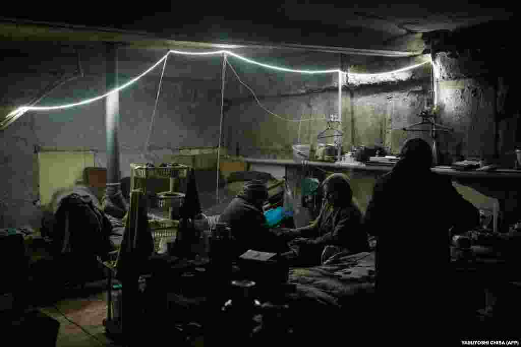 As the vibrations from the shelling above continue, Halyna (center), 83, and Tetyana (left), 68, take turns massaging each other&#39;s hands to keep them warm. They live in this cold basement, which they share with about 20 other people.