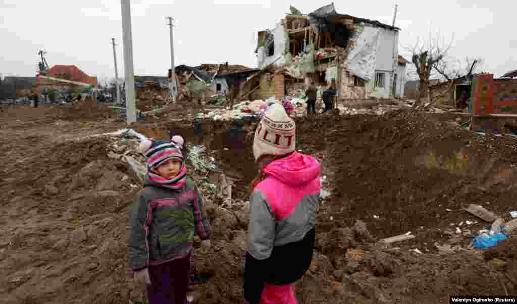 Дети стоят рядом с воронкой от российской ракетной атаки в городе Глеваха под Киевом, 26 января 2023 года.