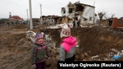 Dy fëmijë ukrainas qëndrojnë pranë një vendi që është goditur nga sulmet ruse në periferi të Kievit. Fotografi ilustruese. 