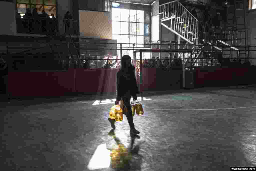 An Afghan laborer carries oil containers provided by a nongovernmental organization for distribution among those in need at a gymnasium in Kabul.