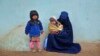 A burqa-clad woman sits with her children along a roadside in Kandahar. 