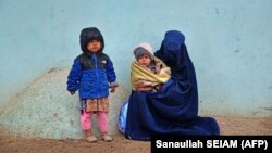 A burqa-clad woman sits with her children along a roadside in Kandahar. 