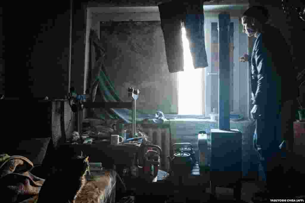 35-летний Александр Луховских смотрит в окно. В окно выведена труба печи, которой он отапливает свою комнату. Семья Александра покинула город. Он остался с котом