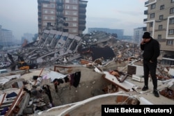 Мужчина, стоящий среди обломков, смотрит на разрушения после землетрясения. Провинция Хатай, Турция, 7 февраля 2023 года