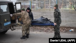 Украинские солдаты забирают тело гражданского мужчины с улицы в Харькове. Он был, как утверждается, убит выстрелом из проезжавшей мимо российской военной автомашины, прорвавшейся в город. 27 февраля 2022 года