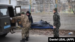 Украинские солдаты забирают тело гражданского мужчины с улицы в Харькове. Он был, как утверждается, убит выстрелом из проезжавшей мимо российской военной автомашины, прорвавшейся в город. 27 февраля 2022 года.