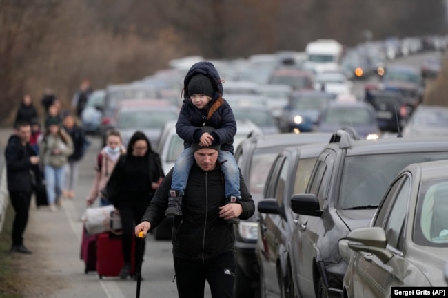 Ukrainian refugees walk beside vehicles lining up to cross the border from Ukraine into Moldova on February 26, 2022.