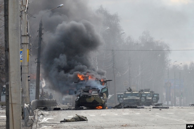 A Russian armored personnel carrier burns next to a soldier's body after fighting in Kharkiv on February 27, 2022.
