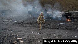 Egy ukrán katona sétál el egy szétlőtt katonai tehergépjármű mellett Kijevben 2022. február 26-án