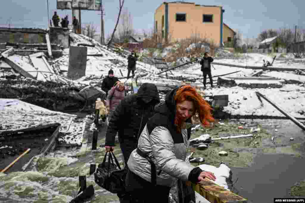 Ukrainian civilians cross a river on a bridge damaged by explosives on Kyiv&#39;s northern front on March 1.&nbsp;