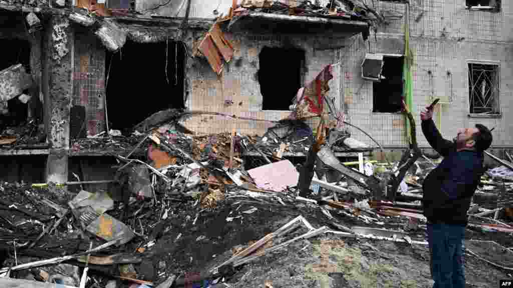 Маж фотографира оштетена зграда во нападите на Киев на 25 февруари 2022
