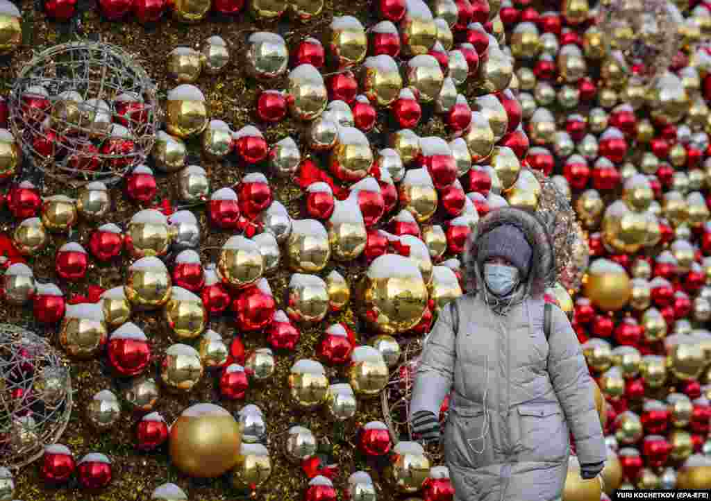 A Russian woman wearing a protective face mask walks on a street festooned with Christmas decorations in Moscow.