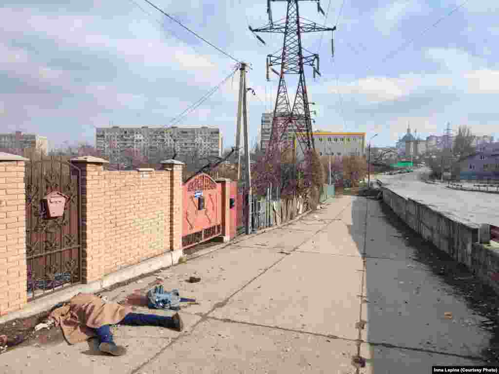 A corpse covered with a blanket lies on a sidewalk in Mariupol.