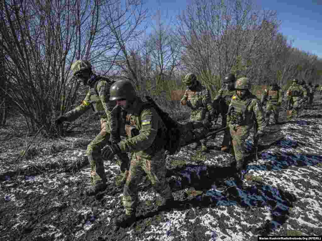 Військові ЗСУ несуть пораненого побратима після штурму населеного пункту, де перебували російські військові. Київщина, 10 березня 2022 року