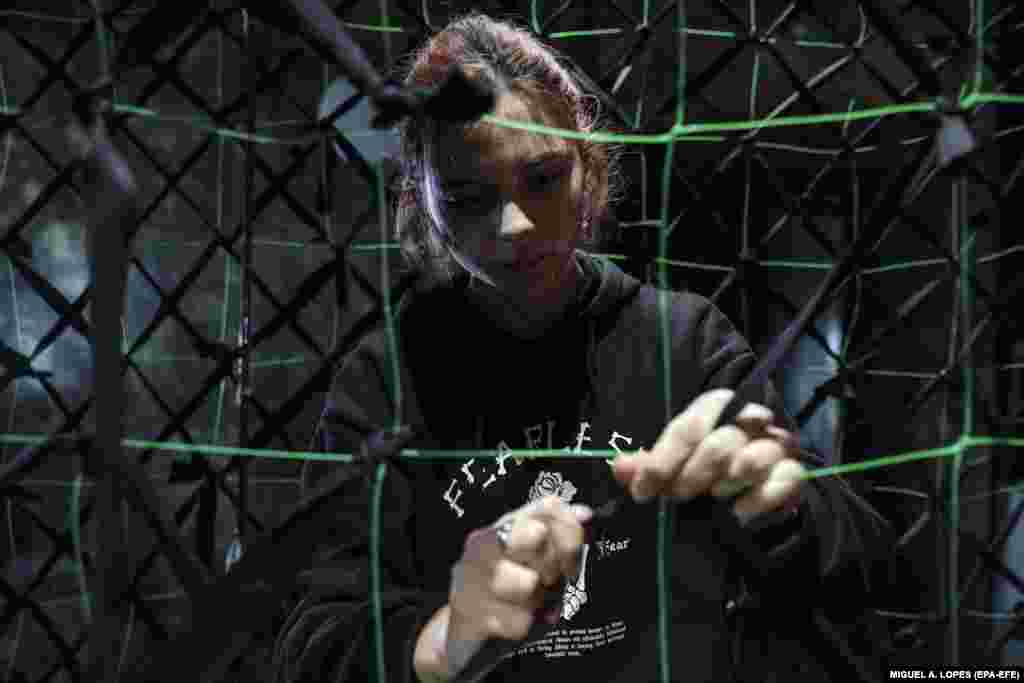 A girl tightens a knot as volunteers produce camouflage netting for the Ukrainian Army to use against the Russian military invasion in Lviv.