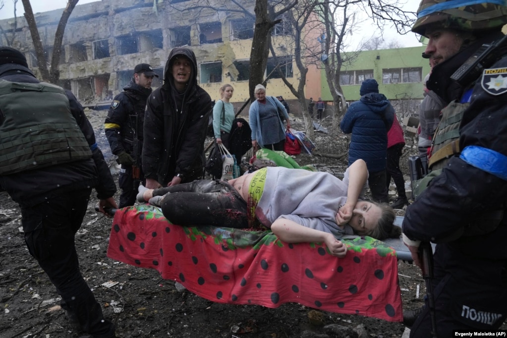 Punonjës të shërbimit të urgjencës dhe vullnetarë duke bartur një grua të lënduar shtatzënë, pas bombardimit rus të spitalit të lindjes në Mariupiol, më 9 mars.
