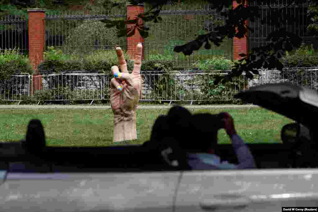 A man takes a picture of a statue of a hand making a rude gesture with its fingernails painted in the colors of Ukraine&#39;s national flag in front of the Russian Embassy in Prague.