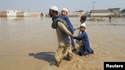 Суу каптаган айылда балдары менен кетип бараткан киши. Пакистан. 30-август, 2022-жыл.