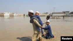  Мужчина идет с детьми среди паводковых вод вдоль дороги после дождей и наводнений в сезон дождей в Новшере, Пакистан, 30 августа 2022 года. 