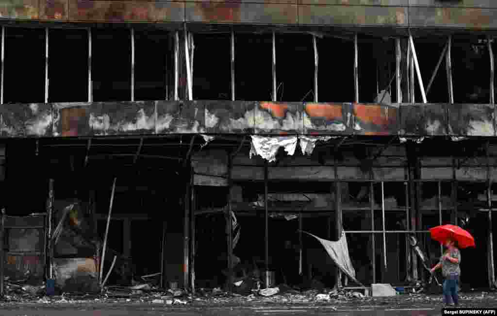 A woman carries an umbrella as she walks past a destroyed shopping mall in Bucha, outside Kyiv.