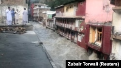 Men watch floodwaters tear through the bazaar in Bahrain, Pakistan, on August 29.